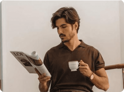 A man holding a coffee cup and reading a magazine.