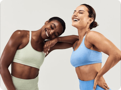 Two women in sports bras smiling for the camera.