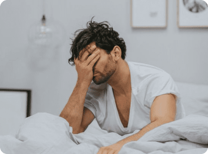 A man in white shirt lying on bed with his head down.