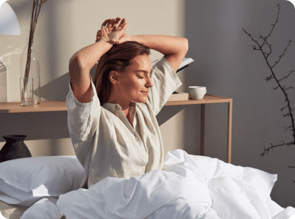 A woman stretching in bed with her hands behind her head.