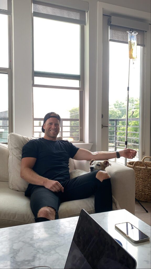 Cheerful man receiving a vitamin IV drip at home, smiling and relaxed.