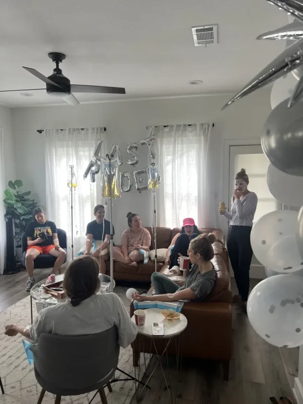 Bachelorette group with Last Ride balloons getting mobile IVs in a living room
